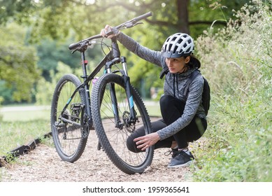 Woman Cyclist  In The Public Park Next To The Bicycle Checking Tires. Common Bike Problems .