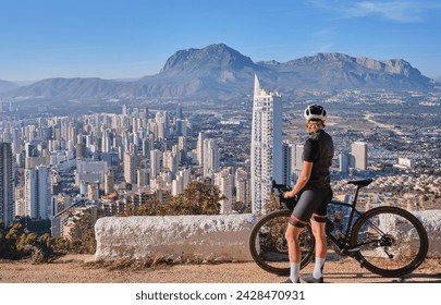 Woman cyclist riding a bike with beautiful view on Benidorm,Costa Blanca,Spain.Woman cyclist wearing cycling kit and helmet.Sports motivation image.Cycling through stunning Spanish mountain landscape. - Powered by Shutterstock