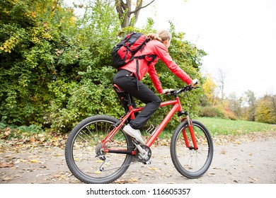 Woman cyclist riding a bike on road in autumn park against the background of green nature
