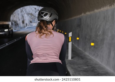 Woman cyclist is riding a bike on road through tunnel close up back view. Empty mountain road. Cycling adventure in Spain. - Powered by Shutterstock