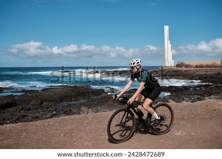 Woman cyclist riding a gravel bicycle a gravel road with beautiful view on Atlantic ocean on Tenerife, Canary Islands, Spain. Sport motivation. Cycling training outdoors in Spain. Cycling adventure.
