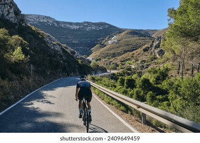 A woman cyclist riding on mountain road. Cyclist on the windy road in mountains. Costa Blanca, Alicante, Spain