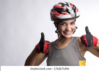 Woman Cyclist With Technical Helmet And Gray Tank Top Makes The Ok Sign With The Thumb Up Isolated On A Light Background