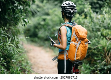 Woman cyclist use smartphone when riding mountain bike on forest trail