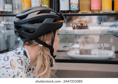 Woman cyclist, wearing full cycling gear, is going to eat piece of pie and drink coffee after a hard ride on her bicycle in a cozy cafe. Healthy lifestyle concept. Cycling adventure. Calp, Alicante - Powered by Shutterstock