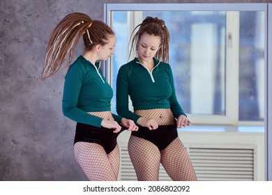 Woman dancer evaluates volume of her body in mirror of dance studio.