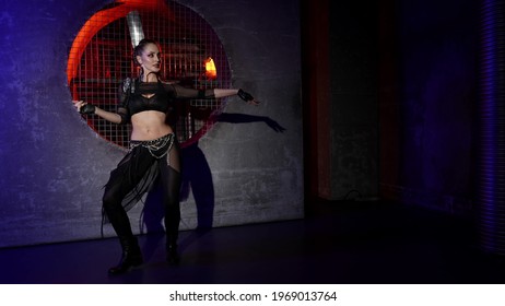 A Woman Dances A Modern Dance In A Darkened Studio, She Is Dressed In A Revealing Suit With An Open Stomach And Is Illuminated By Light. Makes Beautiful Hand Movements.