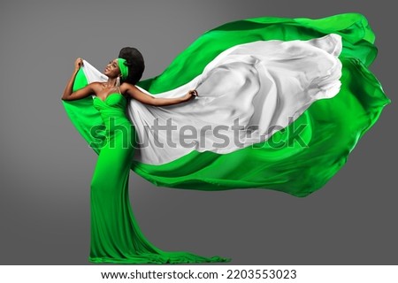 Woman dancing with Nigerian Flag in Green White Dress. Fashion Model with Hair in Long Gown with flying Silk Scarf. Waving Chiffon Fabric over Gray. Nigeria Independence Day