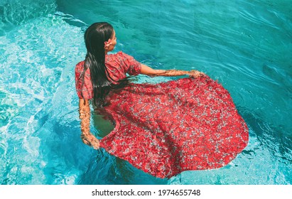 Woman dancing underwater in blue pool in red elegant maxi dress. Beauty fashion model.