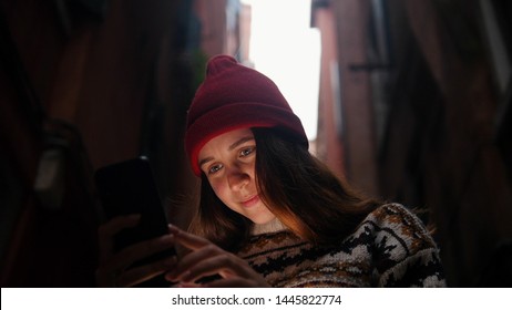 Woman In A Dark Alley Between Buildings. Looks Into Her Phone.