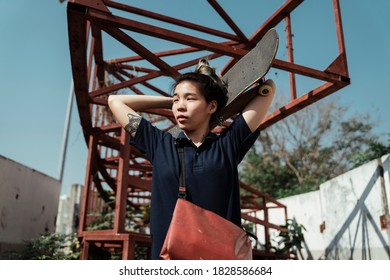 Woman In Dark Blue Polo Shirt Hold The Longboard At Back Of Her Head While Standing Under Red Structure In Sunlight.