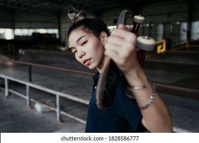 Woman In Dark Blue Polo Shirt Standing And Carry Longboard On Her Shoulder In Medium Shot.