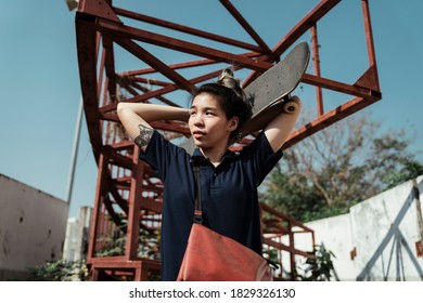 Woman In Dark Blue Polo Shirt Hold The Longboard At Back Of Her Head While Standing Under Red Structure In Sunlight.