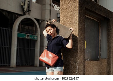 Woman In Dark Blue Polo Shirt Standing In Sunlight Carry The Longboard On Her Shoulder In Summer.