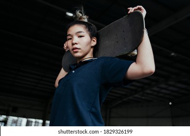 Woman In Dark Blue Polo Shirt Standing And Carry Longboard On Her Shoulder In Medium Shot.