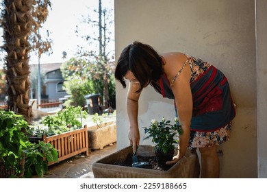 woman with dark hair and colourful dress digging to plant flowers in a pot in house garden - Shutterstock ID 2259188665