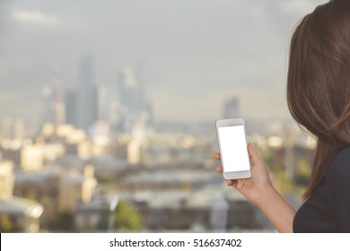 Woman With Dark Hair Holding Blank White Cellular Phone On Blurry City Background. Mock Up