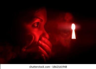 woman in the dark room looks into the keyhole glowing with red mysterious light. She covers her mouth to keep from screaming or being surprised or embarrassment.