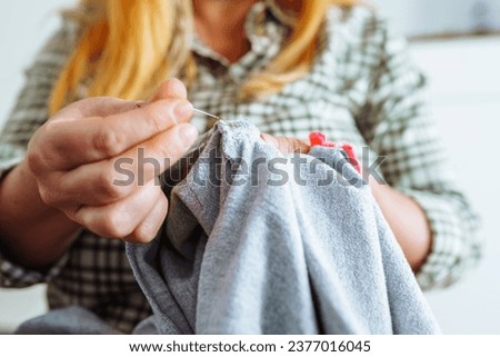 woman darns torn hole in old clothes, gray fabric teenage pajamas. Handmade, DIY clothing repair