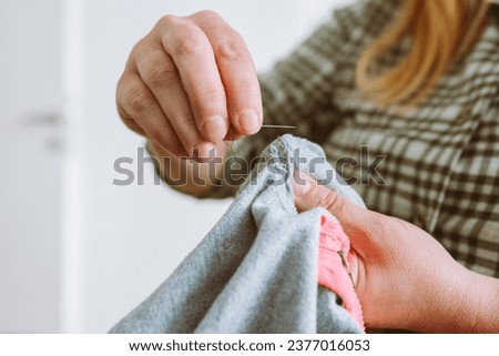 woman darns torn hole in old clothes, gray fabric teenage pajamas. Handmade, DIY clothing repair