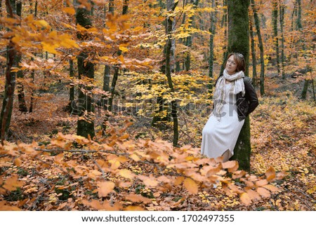 Woman daydreaming in a beech forest in autumn leaning on a tree trunk