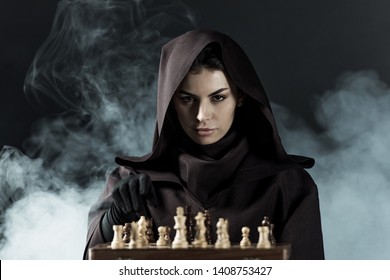 woman in death costume playing chess in smoke on black - Powered by Shutterstock