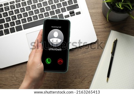 Woman deciding answer incoming call from unknown caller or not at table, closeup. Be careful - fraud