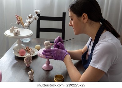 Woman decorates chocolate bear figurine with brush. Selective focus. Image for articles about confectionery.