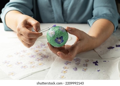 A Woman Decorates A Papier Mache Ball With Pressed Dried Flowers. Homemade Christmas Decoration. Zero Waste New Year. Xmas Handmaded Toy.