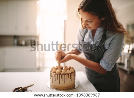 Woman decorating chocolate cake in the kitchen. Female chef making a cake at home.