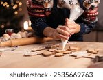 Woman decorating christmas gingerbread cookies with icing on wooden table. Decorating baked christmas cookies. Close-up