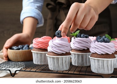 Woman decorating cupcake with fresh blueberry at wooden table, closeup - Powered by Shutterstock