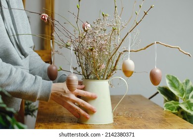 Woman Decorating Easter Flower Arrangement With Hanged Coloured Eggs On Twigs. Spring Easter Home Interior. 