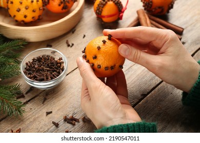 Woman decorating fresh tangerine with cloves at wooden table, closeup. Making Christmas pomander balls