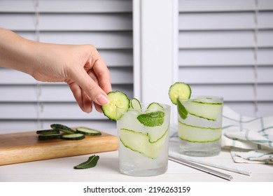 Woman Decorating Glass Of Tasty Fresh Cucumber Water At White Table, Closeup