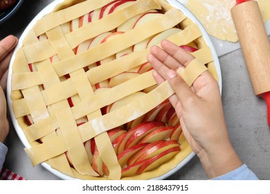 Woman decorating raw apple pie at grey table, top view