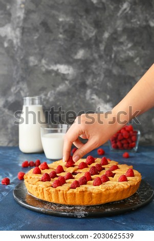 Woman decorating tasty raspberry pie on dark table
