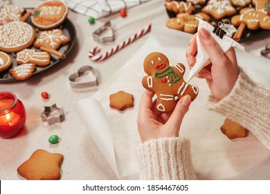 Woman is decorating a traditional gingerbread man. Christmas and New Year holidays mood. Close up view of home kitchen table in preparation