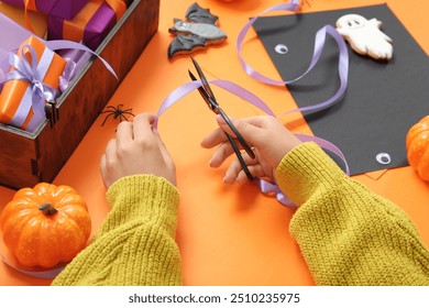 Woman with decorations cutting ribbon for Halloween gift boxes on orange background - Powered by Shutterstock