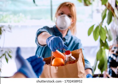 Woman delivering Food in paper bag during Covid 19 outbreak. Female  Volunteer holding groceries in the house porch. Delivery woman in face mask and gloves giving Donating neccessities to a hand