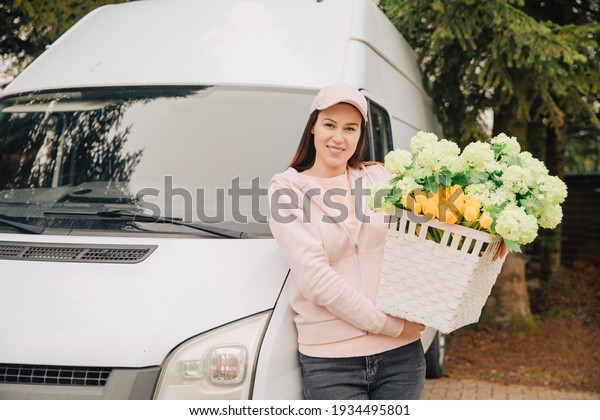 Woman with a\
delivery truck carries a large basket of flowers. Deliver flowers.\
Supply garden plants. Gardener company brings flowers home.\
Delivery woman carries\
flowers	