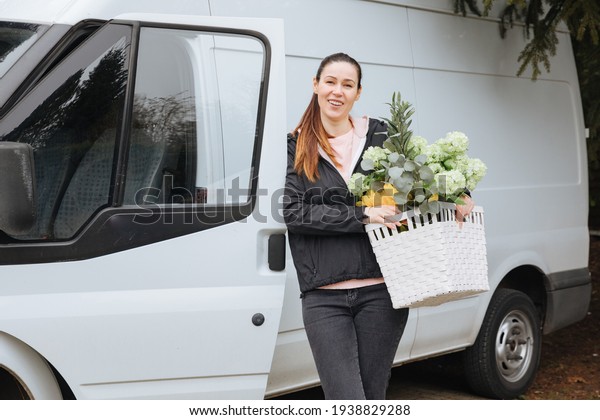 Woman with a\
delivery truck carries a large basket of flowers. Deliver flowers.\
Supply garden plants. Gardener company brings flowers home.\
Delivery woman carries\
flowers