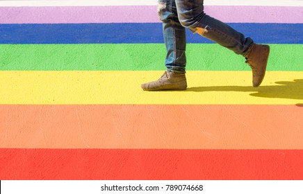 Frauen in Denim und Moccasinen, die auf einem farbigen Kreuzweg unter der LGBT-Flagge zu Fuß gehen
