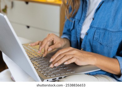 Woman in denim shirt typing on laptop at home, focusing on work. Remote working, home office, technology, concentration, productivity, casual - Powered by Shutterstock