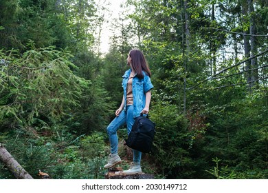 Woman In Denim Suit In Boots With Photo Backpack Is Engaged In Hiking In Forest. Unrecognizable Caucasian Young Woman Walking In Nature In Park. Journey Alone Back View