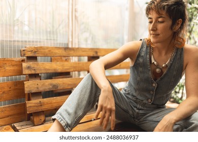 A woman in a denim vest sits on a wooden bench. She is wearing a necklace and has red hair - Powered by Shutterstock