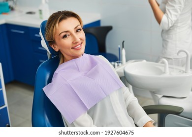 Woman in a dental office having a seat in a medical chair with cloth on her chest and smiling - Powered by Shutterstock