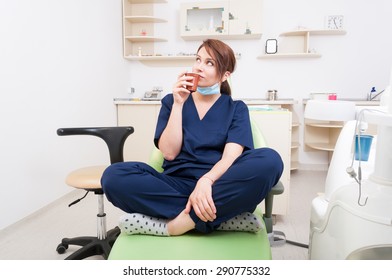 Woman dentist doctor thinking and having a coffee break in dental office sitting on dentist chair