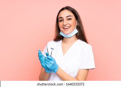 Woman dentist holding tools isolated on pink background applauding - Powered by Shutterstock