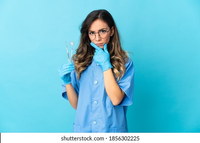 Woman dentist holding tools over isolated on blue background thinking
